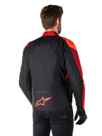 Widok z tyłu na mężczyznę ubranego w kurtkę Alpinestars T-Jaws V4 Waterproof w kolorze Black Red Fluo Dark Red, z jaskrawoczerwonymi akcentami na ramionach i rękawach, neonowym czerwonym logo Alpinestars na dole pleców, w zestawieniu z czarnymi spodniami i rękawicami.