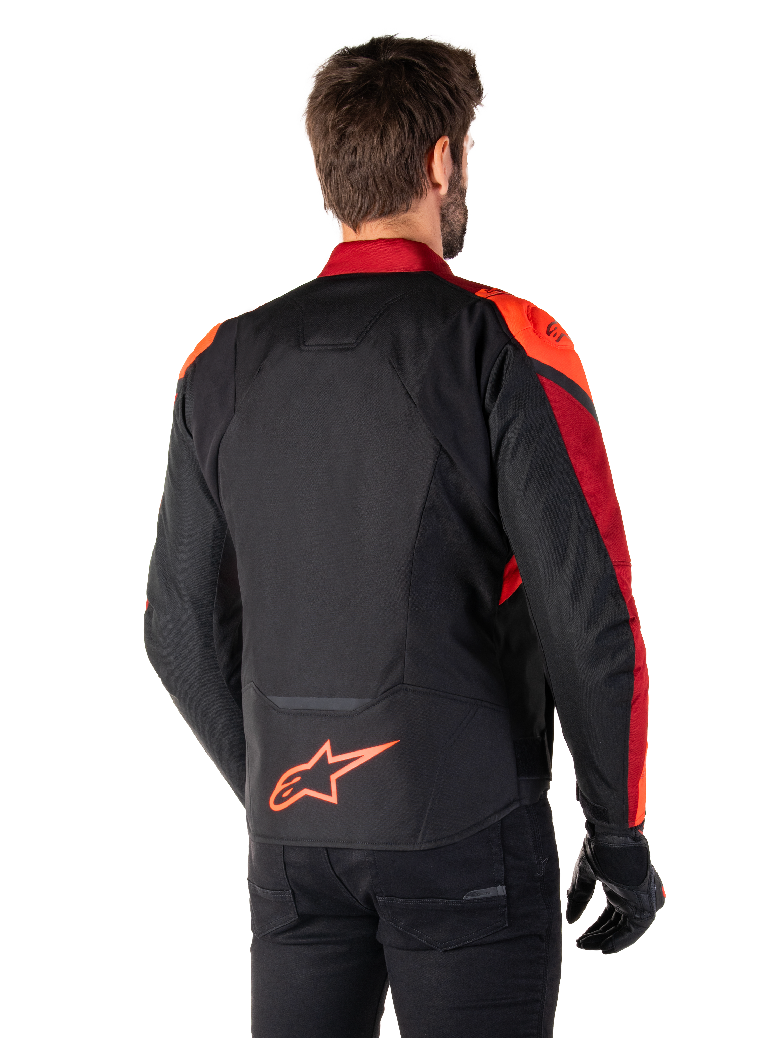 Widok z tyłu na mężczyznę ubranego w kurtkę Alpinestars T-Jaws V4 Waterproof w kolorze Black Red Fluo Dark Red, z jaskrawoczerwonymi akcentami na ramionach i rękawach, neonowym czerwonym logo Alpinestars na dole pleców, w zestawieniu z czarnymi spodniami i rękawicami.