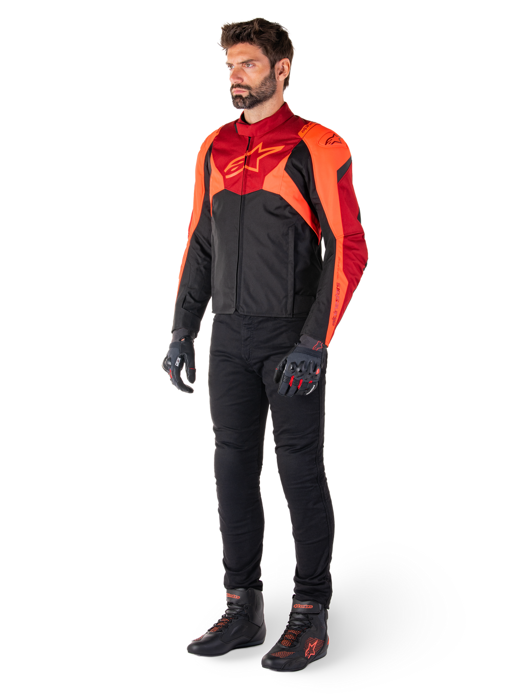 Męski motocyklista w kurtce Alpinestars T-Jaws V4 Waterproof w kolorze Black Red Fluo Dark Red, w zestawieniu z czarnymi spodniami motocyklowymi, rękawicami i butami do jazdy, o sportowym tekstylnym kroju z wyraźnym logo na klatce piersiowej i agresywnej sylwetce.