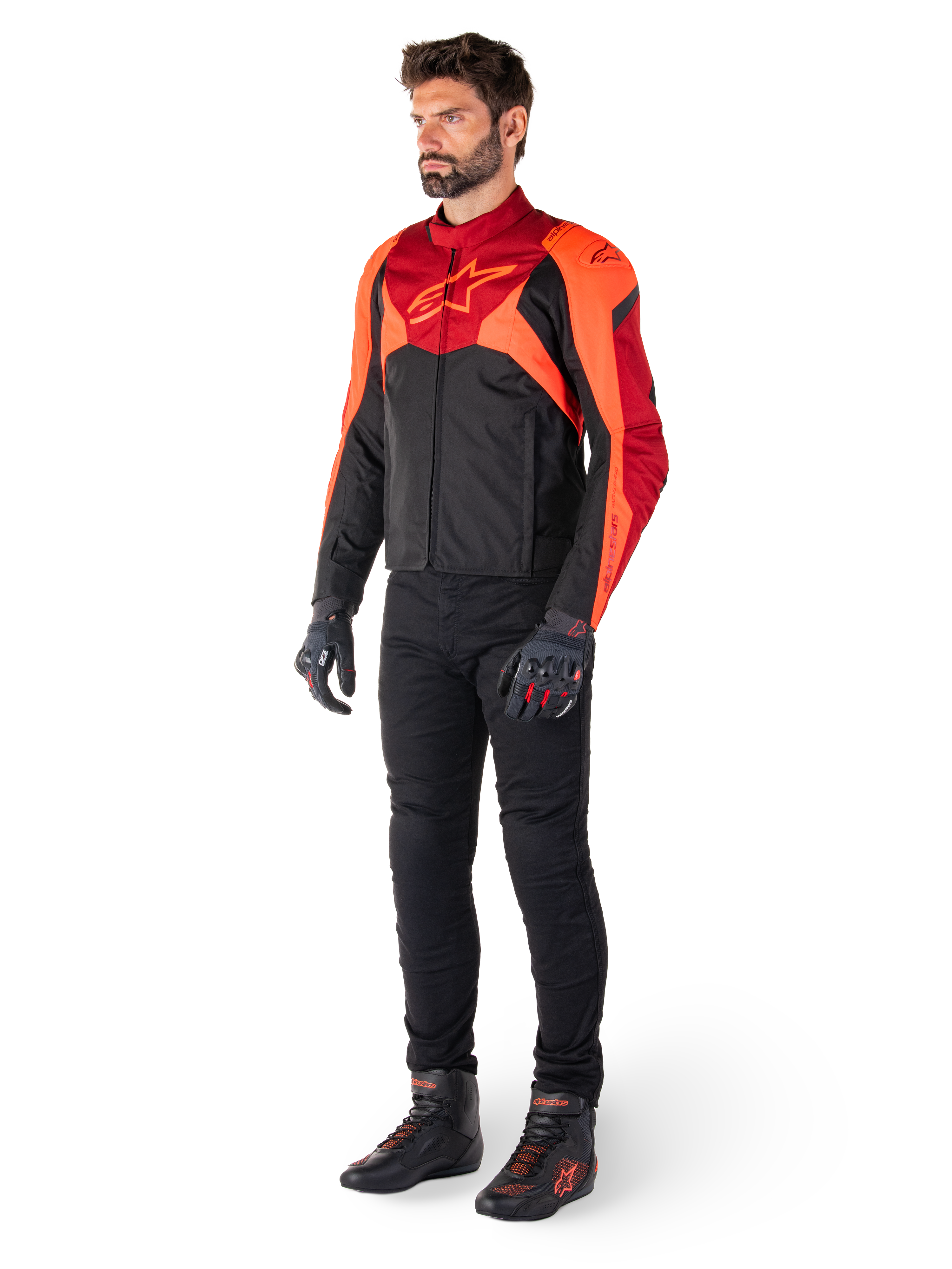 Męski motocyklista w kurtce Alpinestars T-Jaws V4 Waterproof w kolorze Black Red Fluo Dark Red, w zestawieniu z czarnymi spodniami motocyklowymi, rękawicami i butami do jazdy, o sportowym tekstylnym kroju z wyraźnym logo na klatce piersiowej i agresywnej sylwetce.