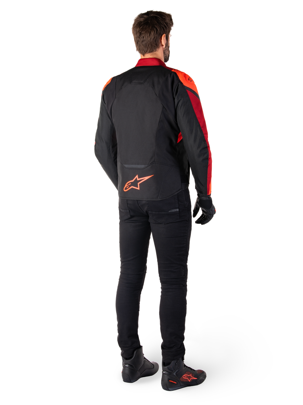 Alpinestars T-Jaws V4 Waterproof Jacket w kolorze Black Red Fluo Dark Red, widok z tyłu motocyklisty ubranego w kurtkę tekstylną, czarne spodnie i buty motocyklowe, z wyraźnym czerwonym logo Alpinestars w dolnej części pleców.