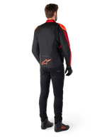 Alpinestars T-Jaws V4 Waterproof Jacket w kolorze Black Red Fluo Dark Red, widok z tyłu motocyklisty ubranego w kurtkę tekstylną, czarne spodnie i buty motocyklowe, z wyraźnym czerwonym logo Alpinestars w dolnej części pleców.