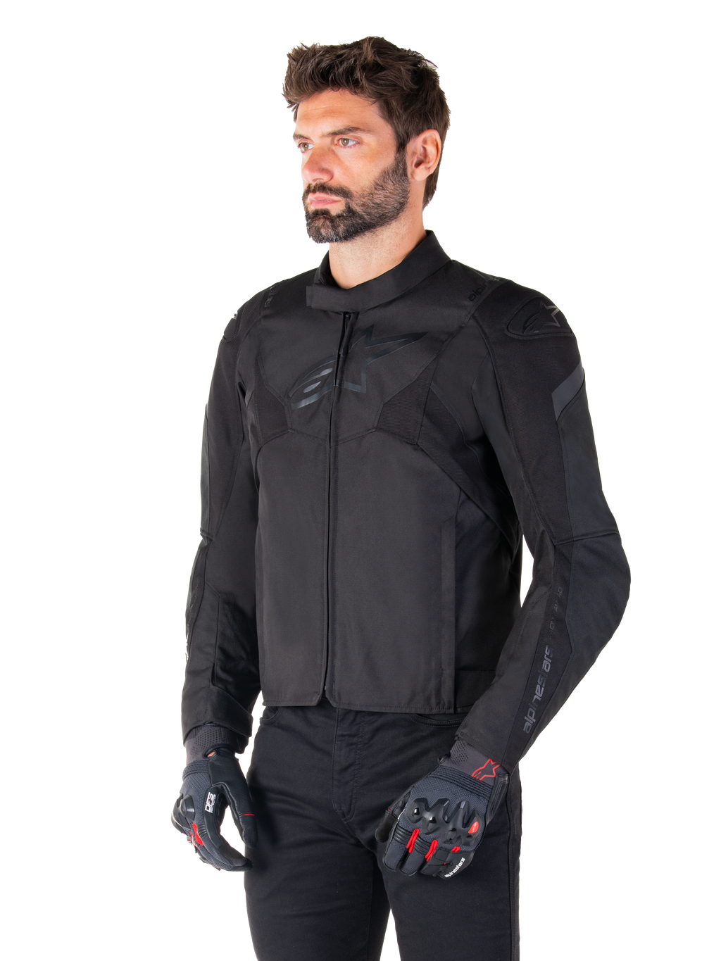 Mężczyzna w wodoodpornej kurtce Alpinestars T-Jaws V4 w kolorze Black Black, w czarnych spodniach i rękawicach ochronnych, charakteryzującej się sportowym krojem, subtelnymi logo Alpinestars na klatce piersiowej i ramionach oraz zaawansowaną konstrukcją tekstylną.