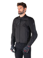 Mężczyzna w wodoodpornej kurtce Alpinestars T-Jaws V4 w kolorze Black Black, w czarnych spodniach i rękawicach ochronnych, charakteryzującej się sportowym krojem, subtelnymi logo Alpinestars na klatce piersiowej i ramionach oraz zaawansowaną konstrukcją tekstylną.