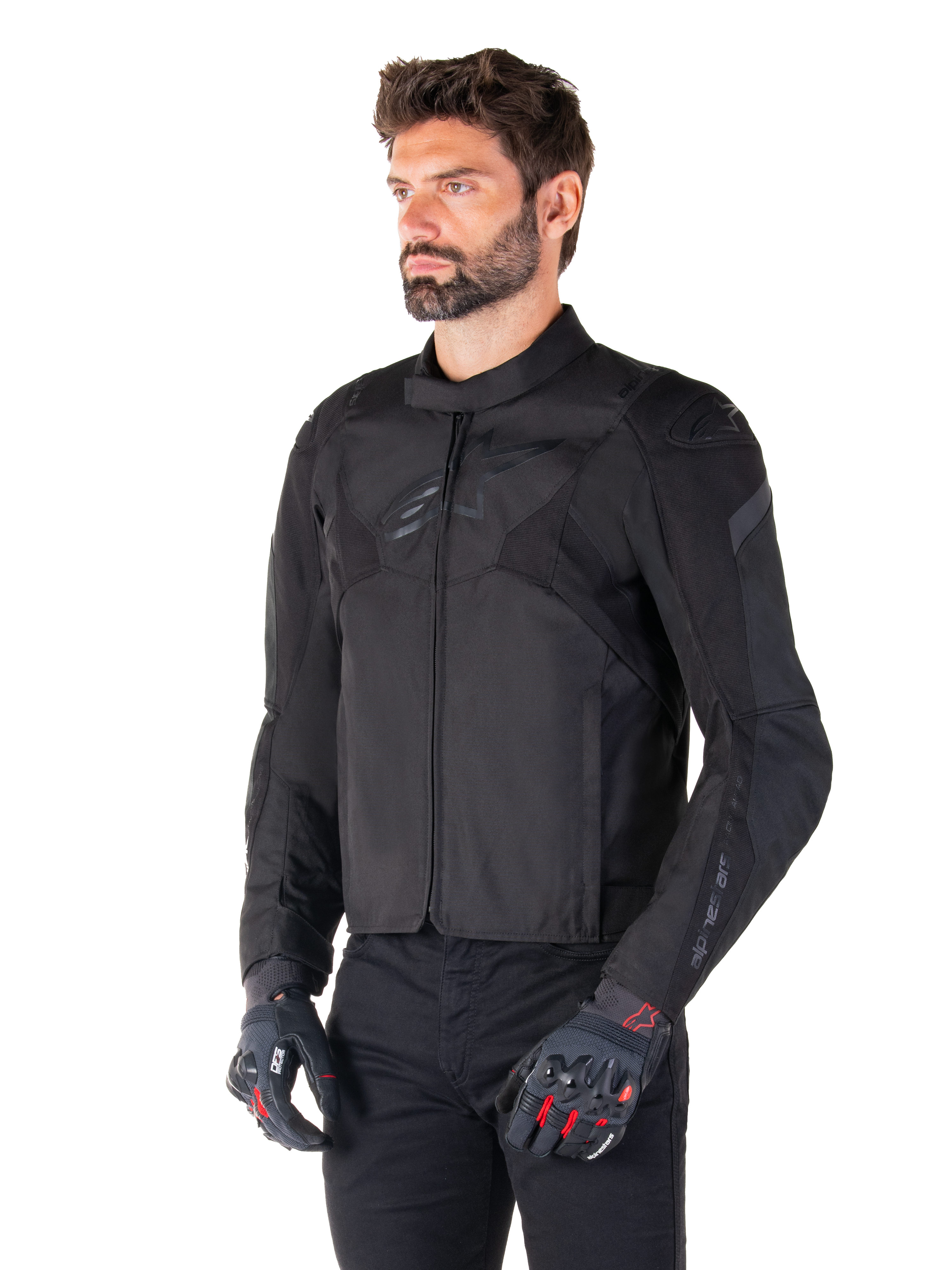 Mężczyzna w wodoodpornej kurtce Alpinestars T-Jaws V4 w kolorze Black Black, w czarnych spodniach i rękawicach ochronnych, charakteryzującej się sportowym krojem, subtelnymi logo Alpinestars na klatce piersiowej i ramionach oraz zaawansowaną konstrukcją tekstylną.