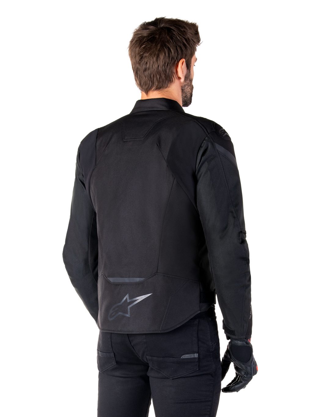 Kurtka wodoodporna Alpinestars T-Jaws V4, czarna, widok z tyłu na modelu, odblaskowe logo Alpinestars w dolnej części pleców, przedłużony tył dla lepszej osłony, sportowy tekstylny design z tonalnymi panelami, noszona z czarnymi rękawicami motocyklowymi