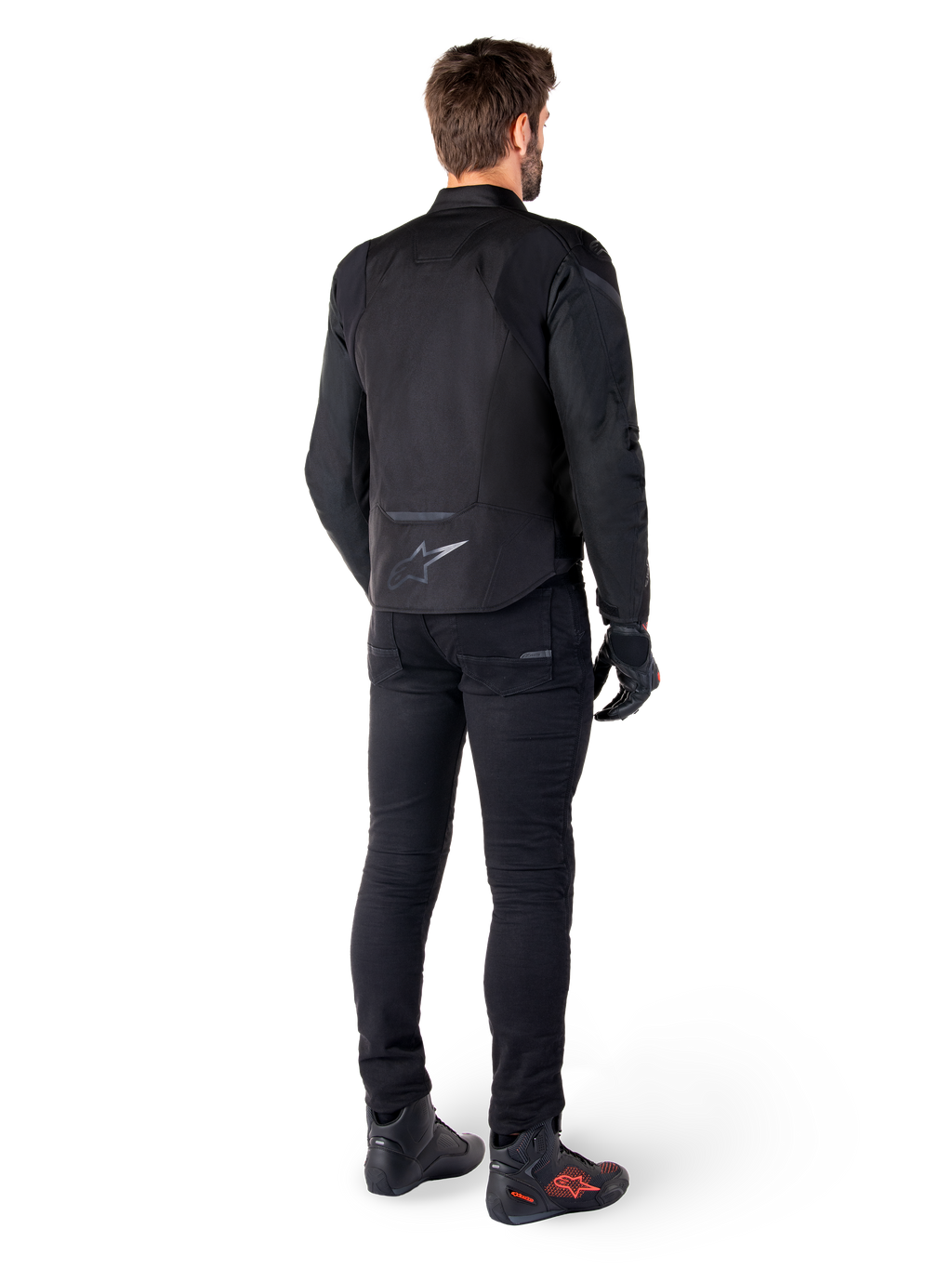 Alpinestars T-Jaws V4 Waterproof Jacket, czarna, widok z tyłu na modelu w czarnych spodniach i butach motocyklowych, sportowa konstrukcja tekstylna, logo Alpinestars w dolnej części pleców