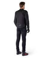 Alpinestars T-Jaws V4 Waterproof Jacket, czarna, widok z tyłu na modelu w czarnych spodniach i butach motocyklowych, sportowa konstrukcja tekstylna, logo Alpinestars w dolnej części pleców