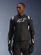 Alpinestars T-SP 1 V2 Waterproof Jacket, sportowa tekstylna kurtka motocyklowa, czarno-biała z subtelnymi czerwonymi detalami, noszona przez modela z dopasowanymi rękawicami i spodniami, białe logo Alpinestars na piersi, branding T-SP-1, ochronna sylwetka do jazdy szosowej