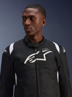 Kurtka Alpinestars T-SP 1 V2 Waterproof prezentowana przez modela, czarno-biała tekstylna kurtka motocyklowa, duże białe logo Alpinestars i branding T-SP-1 na klatce piersiowej, sportowy design z ochronnymi ślizgaczami na ramionach