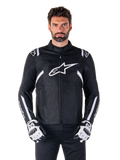 Alpinestars T-SPS V2 Waterproof Jacket w kolorze czarno-białym, widok z przodu na modelu, wodoodporna tekstylna kurtka motocyklowa z białymi pasami na ramionach i rękawach, duże białe logo Alpinestars na piersi, noszona z ochronnymi rękawicami motocyklowymi, smukła sylwetka inspirowana sportem