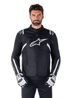 Alpinestars T-SPS V2 Waterproof Jacket w kolorze czarno-białym, widok z przodu na modelu, wodoodporna tekstylna kurtka motocyklowa z białymi pasami na ramionach i rękawach, duże białe logo Alpinestars na piersi, noszona z ochronnymi rękawicami motocyklowymi, smukła sylwetka inspirowana sportem