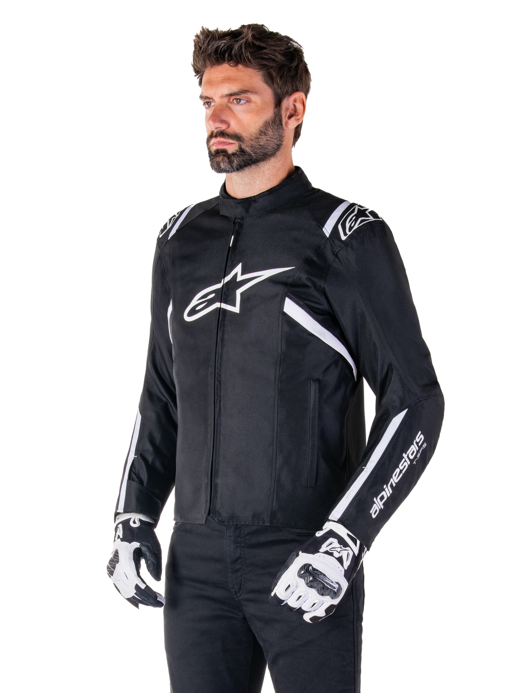 Kurtka Alpinestars T-SPS V2 Waterproof, czarno-biała, noszona przez modela w pasujących rękawicach motocyklowych, tekstylna kurtka o sportowym kroju z białym logo Alpinestars na piersi i ramionach, branding "alpinestars T-SPS" na rękawie, stylowa odzież motocyklowa inspirowana wyścigami