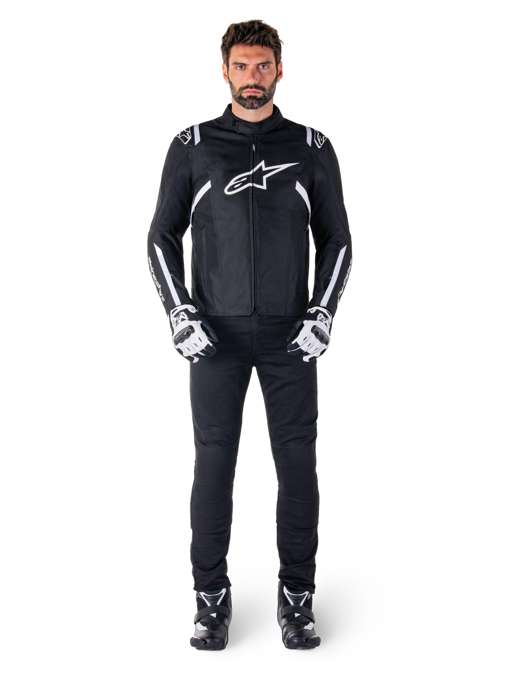 Alpinestars T-SPS V2 Waterproof Jacket, czarno-biała, noszona przez modela z czarnymi spodniami i dopasowanymi rękawicami, białe logo Alpinestars na klatce piersiowej i akcenty na rękawach, sportowy krój do jazdy motocyklowej w każdych warunkach pogodowych
