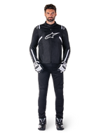 Alpinestars T-SPS V2 Waterproof Jacket, czarno-biała, noszona przez modela z czarnymi spodniami i dopasowanymi rękawicami, białe logo Alpinestars na klatce piersiowej i akcenty na rękawach, sportowy krój do jazdy motocyklowej w każdych warunkach pogodowych