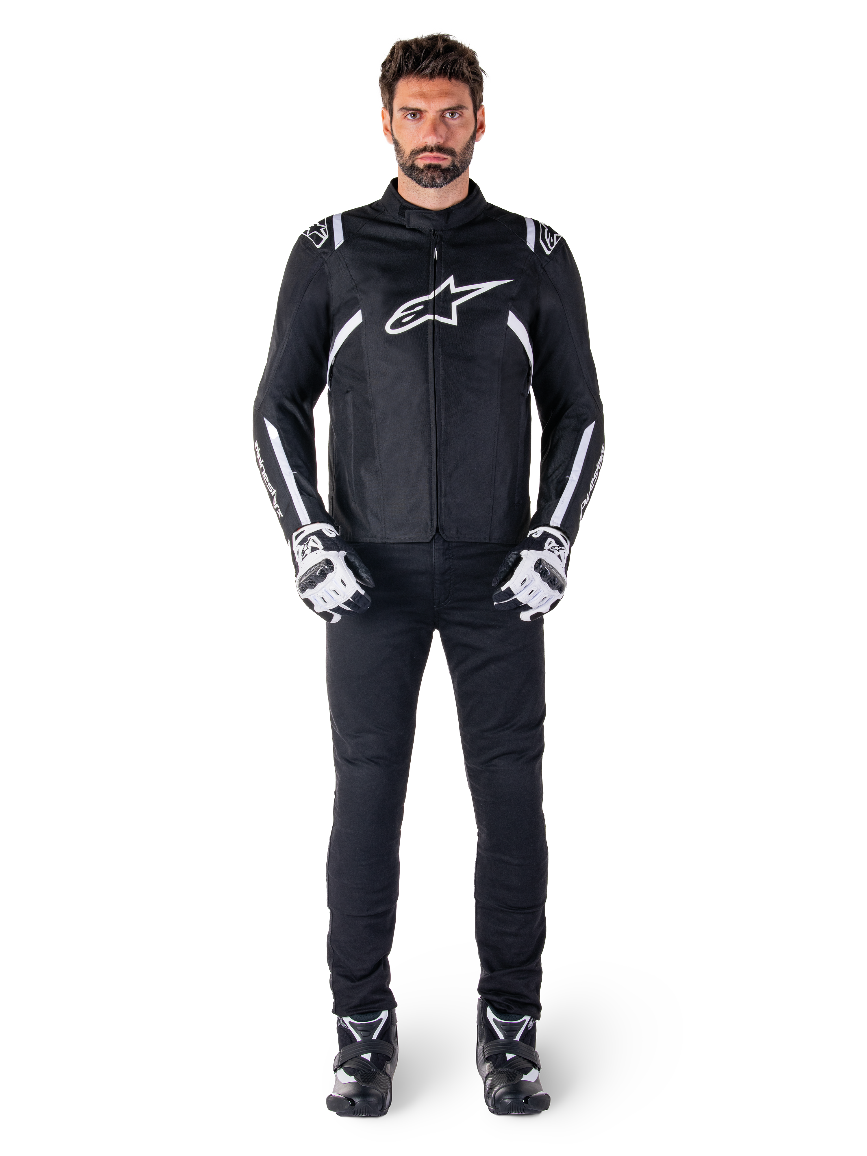 Alpinestars T-SPS V2 Waterproof Jacket, czarno-biała, noszona przez modela z czarnymi spodniami i dopasowanymi rękawicami, białe logo Alpinestars na klatce piersiowej i akcenty na rękawach, sportowy krój do jazdy motocyklowej w każdych warunkach pogodowych