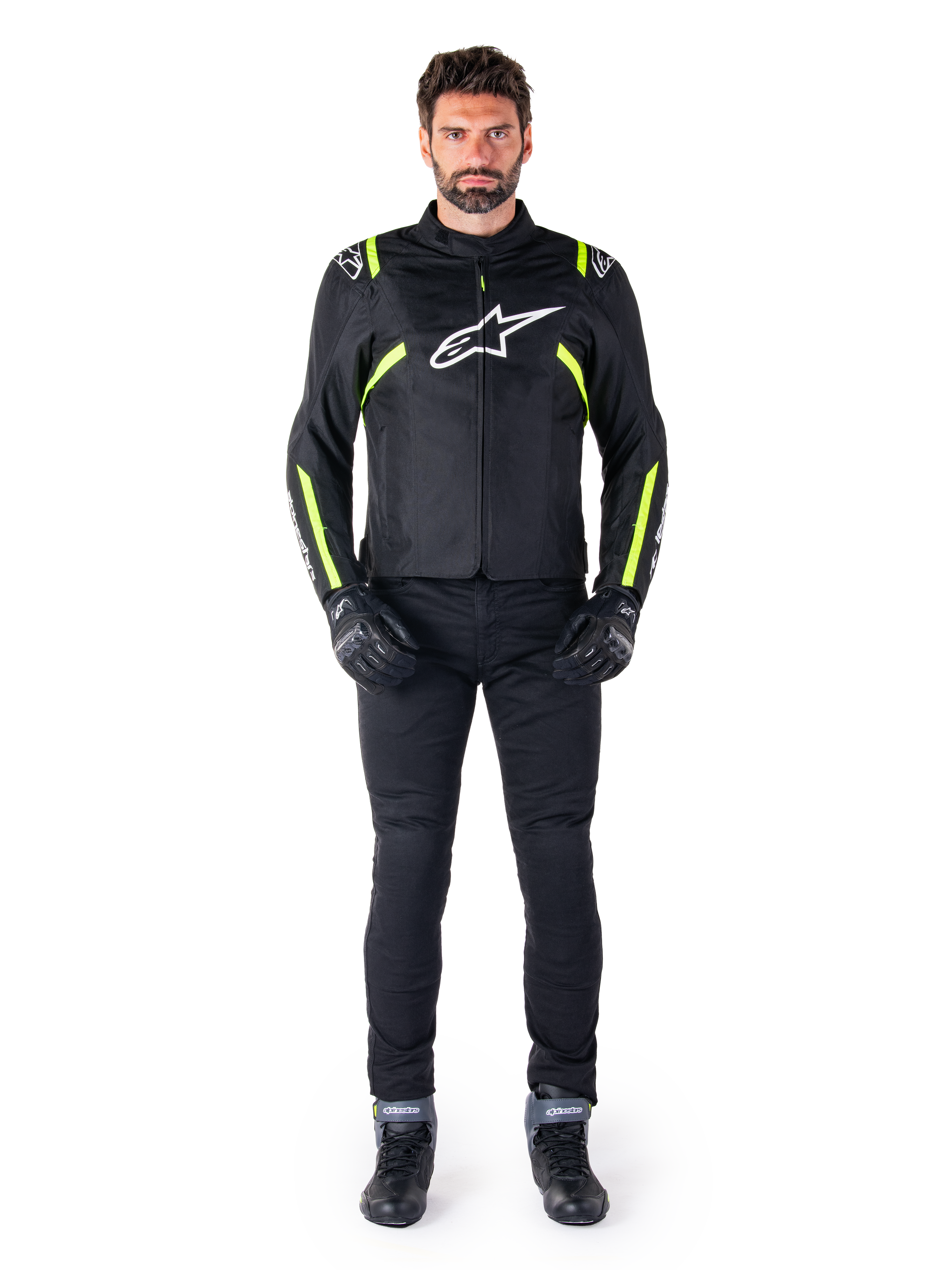 Alpinestars T-SPS V2 Waterproof Jacket, Black White and Yellow Fluo, worn by a model with black riding pants and gloves, featuring a white Alpinestars logo on the chest and fluorescent accents on shoulders and sleeves, sport-cut motorcycle gear