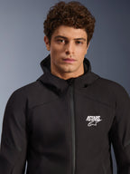Alpinestars Aeroshell Waterproof Jacket, męski model w czarnej kurtce softshell z kapturem, białe logo ASTARS na piersi, wodoodporny zamek błyskawiczny z przodu, nowoczesny portret studyjny, odzież motocyklowa