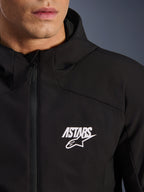 Alpinestars Aeroshell Waterproof Jacket, czarna motocyklowa kurtka typu softshell, zbliżenie na klatkę piersiową z białym logo gwiazdy ASTARS i wodoodpornym przednim zamkiem błyskawicznym, zintegrowany kaptur, nowoczesny sportowy design