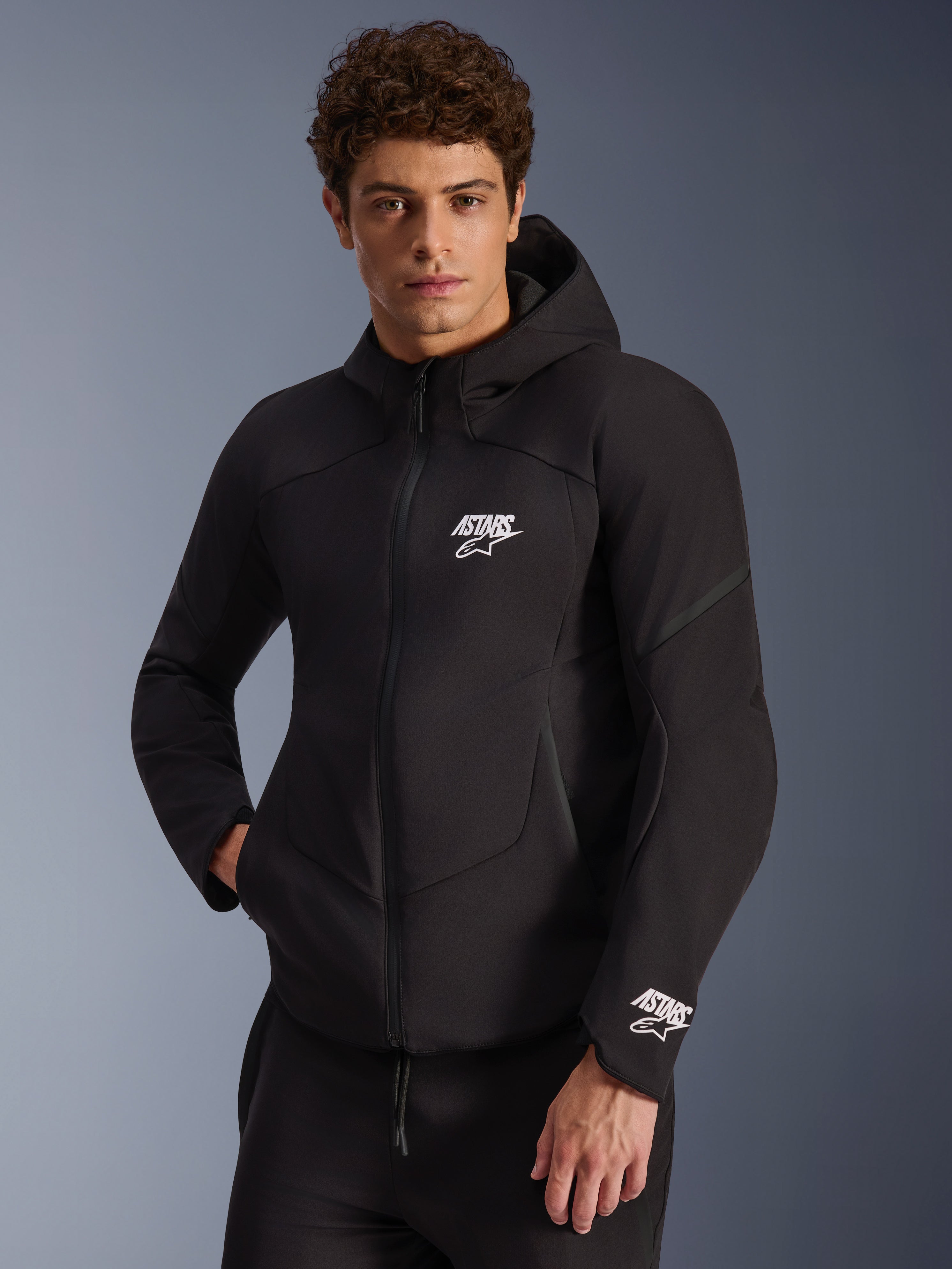 Alpinestars Aeroshell Waterproof Jacket, czarna motocyklowa kurtka softshell z kapturem, białe logo ASTARS na piersi i mankiecie, nowoczesny krój ze zintegrowanym kapturem i wodoodpornym zamkiem, odzież do jazdy miejskiej inspirowana stylem sportowym