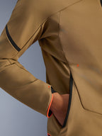Zbliżenie na kurtkę Alpinestars Aeroshell Waterproof Jacket, ciemne khaki z czarnymi i pomarańczowymi akcentami fluo, detal ukrytej kieszeni na zamek i mankietu rękawa, elastyczny materiał softshell do jazdy motocyklem