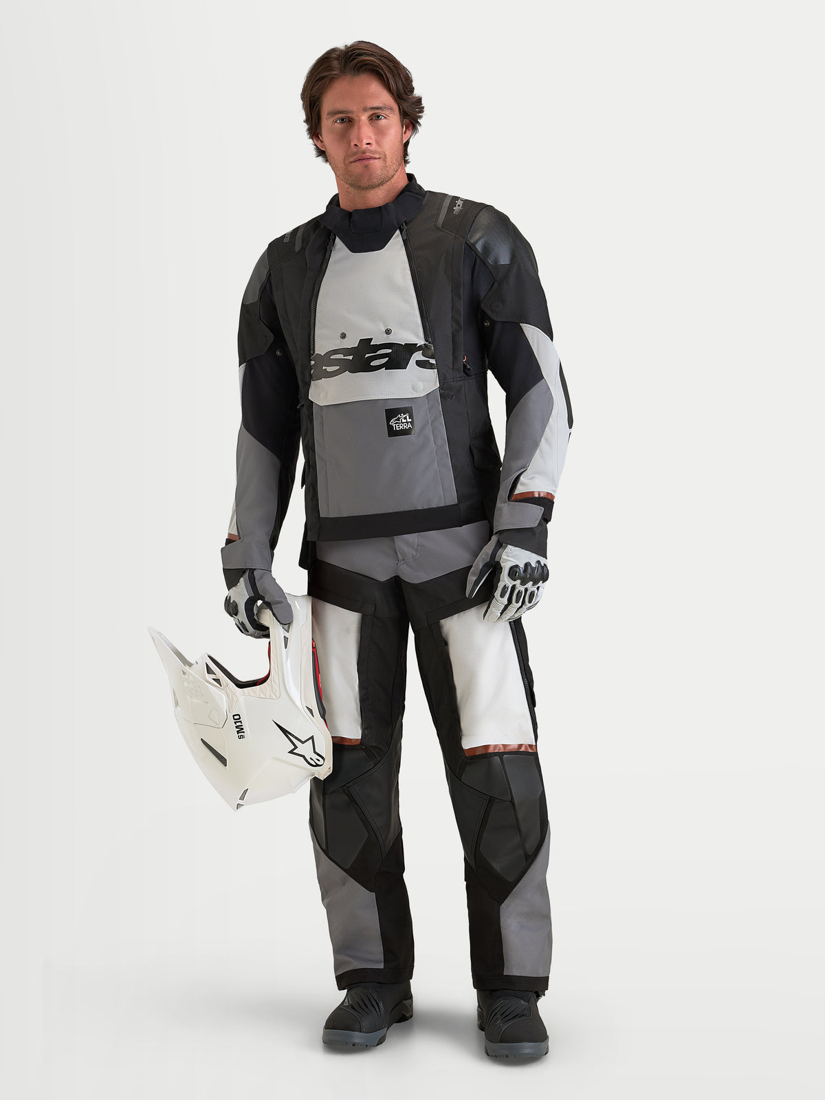 Alpinestars Harok V2 Drystar, męska kurtka motocyklowa adventure, ciemnoszara, jasnoszara i czarna, wodoodporna konstrukcja tekstylna z certyfikowaną ochroną CE, prezentowana przez modela trzymającego biały kask