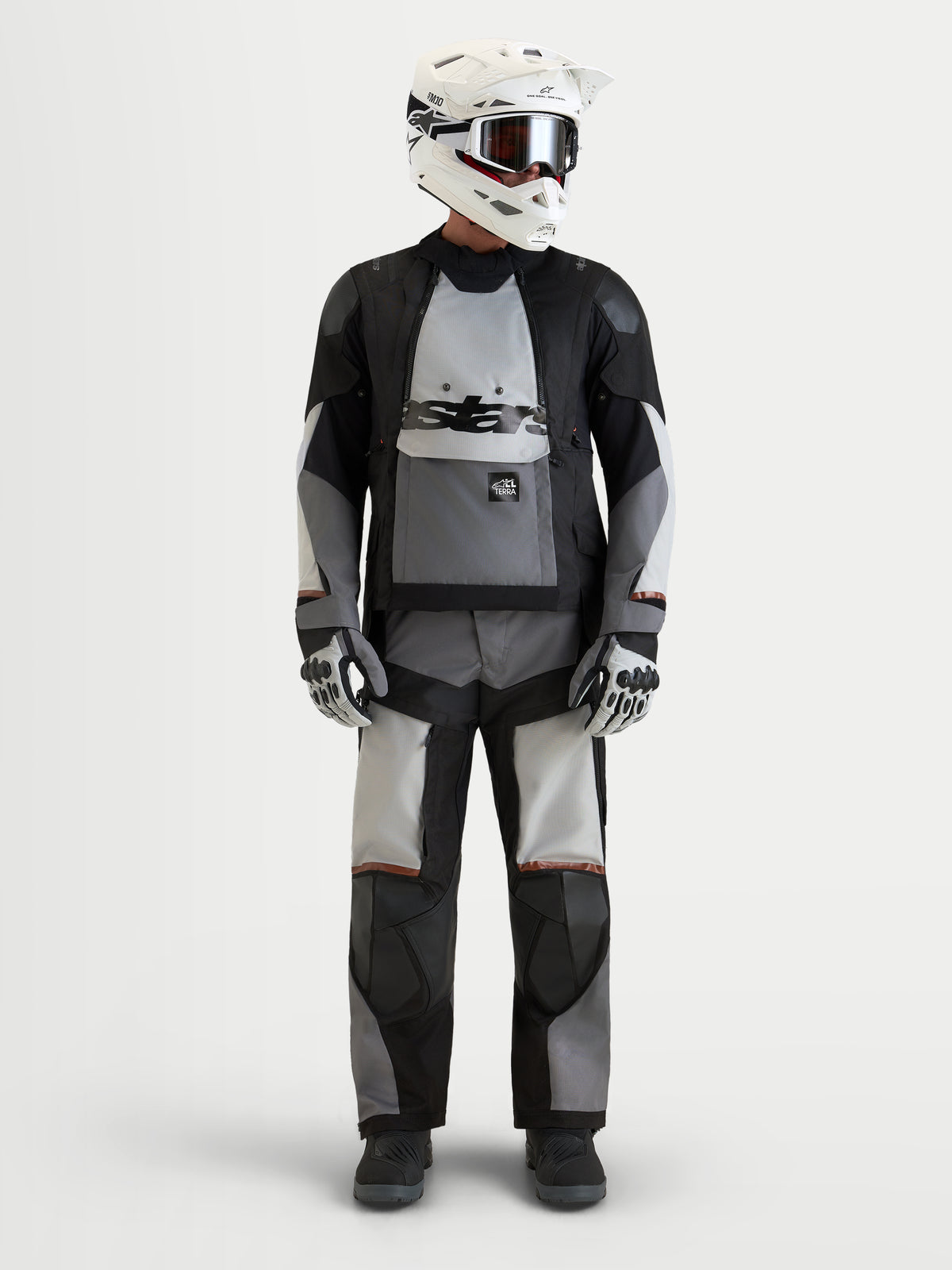 Alpinestars Harok V2 Drystar Gear Set, czarno-szary turystyczny zestaw odzieży motocyklowej adventure, na modelu z białym kaskiem i rękawicami, wodoodporna odzież na każdą pogodę