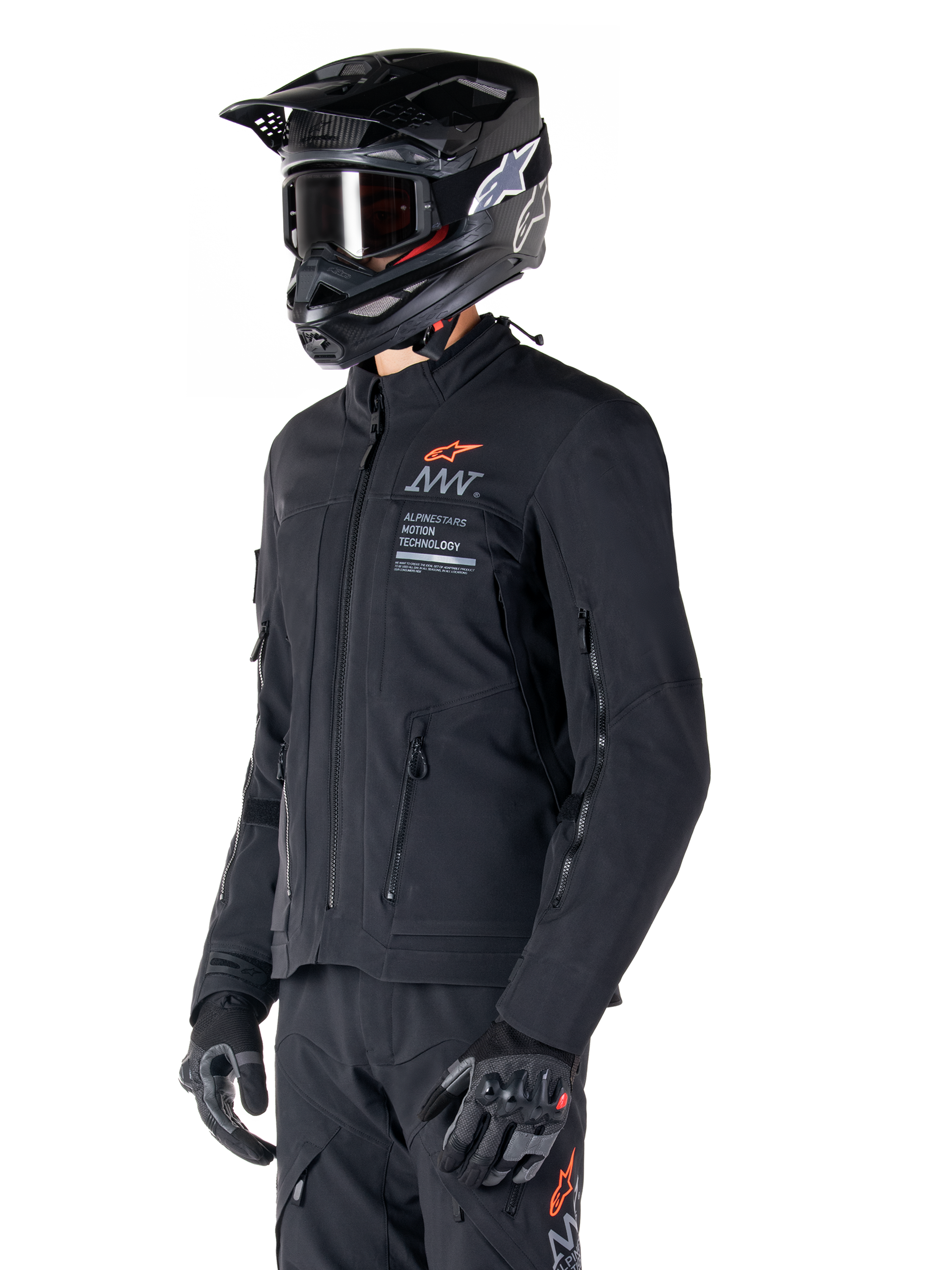Kurtka Alpinestars AMT-8 Stretch Drystar® XF, czarna, noszona przez motocyklistę z dopasowanymi spodniami adventure i rękawicami, czarny kask motocrossowy i gogle, zapinane na zamek otwory wentylacyjne na klatce piersiowej i rękawach, branding Alpinestars Motion Technology z pomarańczowym logo, wysokiej jakości odzież adventure-touring