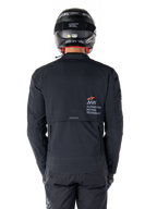 Kurtka Alpinestars AMT-8 Stretch Drystar® XF, widok z tyłu, czarna, noszona z czarnym kaskiem i spodniami, z logo Alpinestars Motion Technology na plecach, design adventure touring z ergonomicznego elastycznego materiału.