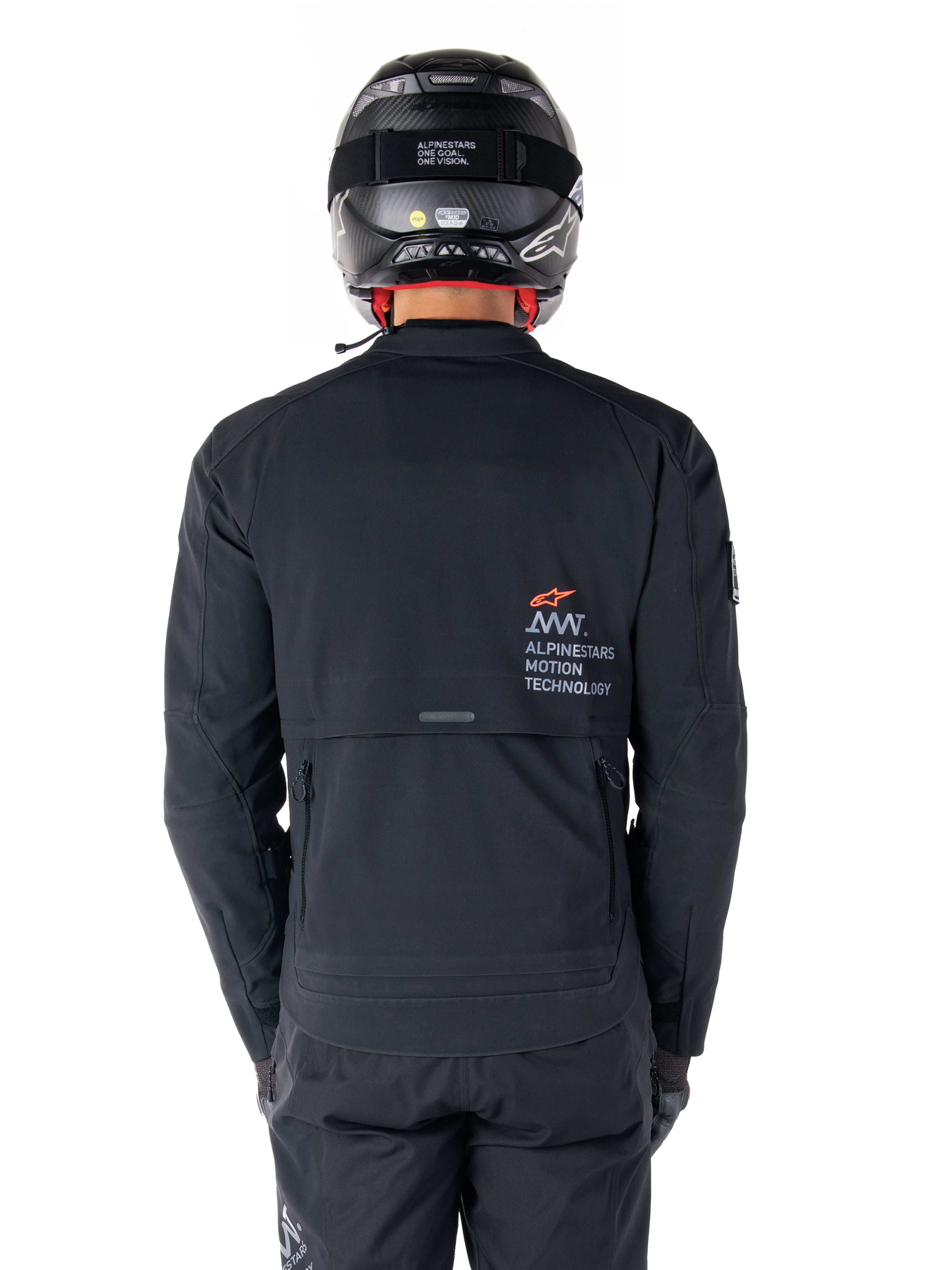 Kurtka Alpinestars AMT-8 Stretch Drystar® XF, widok z tyłu, czarna, noszona z czarnym kaskiem i spodniami, z logo Alpinestars Motion Technology na plecach, design adventure touring z ergonomicznego elastycznego materiału.