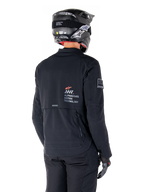 Widok z tyłu motocyklisty w czarnej kurtce Alpinestars AMT-8 Stretch Drystar® XF, z logo „AMT Alpinestars Motion Technology” na plecach, techniczną wentylacją na zamki, w czarnym kasku motocyklowym i rękawicach