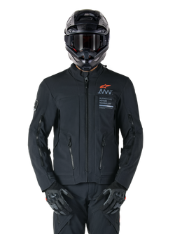 Alpinestars AMT-8 Stretch Drystar® XF Jacket, Black Motorcycle Jacket, featuring orange Alpinestars logo and grey AMT branding, high collar with front zipper and vents, worn with black helmet and gloves, protective adventure touring gear