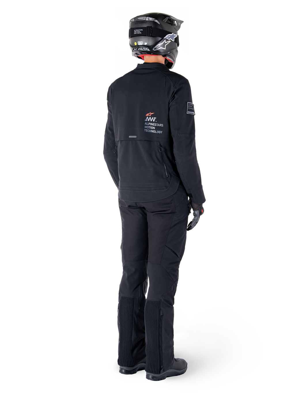 Kurtka Alpinestars AMT-8 Stretch Drystar® XF, czarna, widok z tyłu motocyklisty ubranego w kurtkę, pasujące czarne spodnie i czarny kask, z logo „Alpinestars Motion Technology” na plecach, techniczny elastyczny materiał do jazdy motocyklowej typu adventure