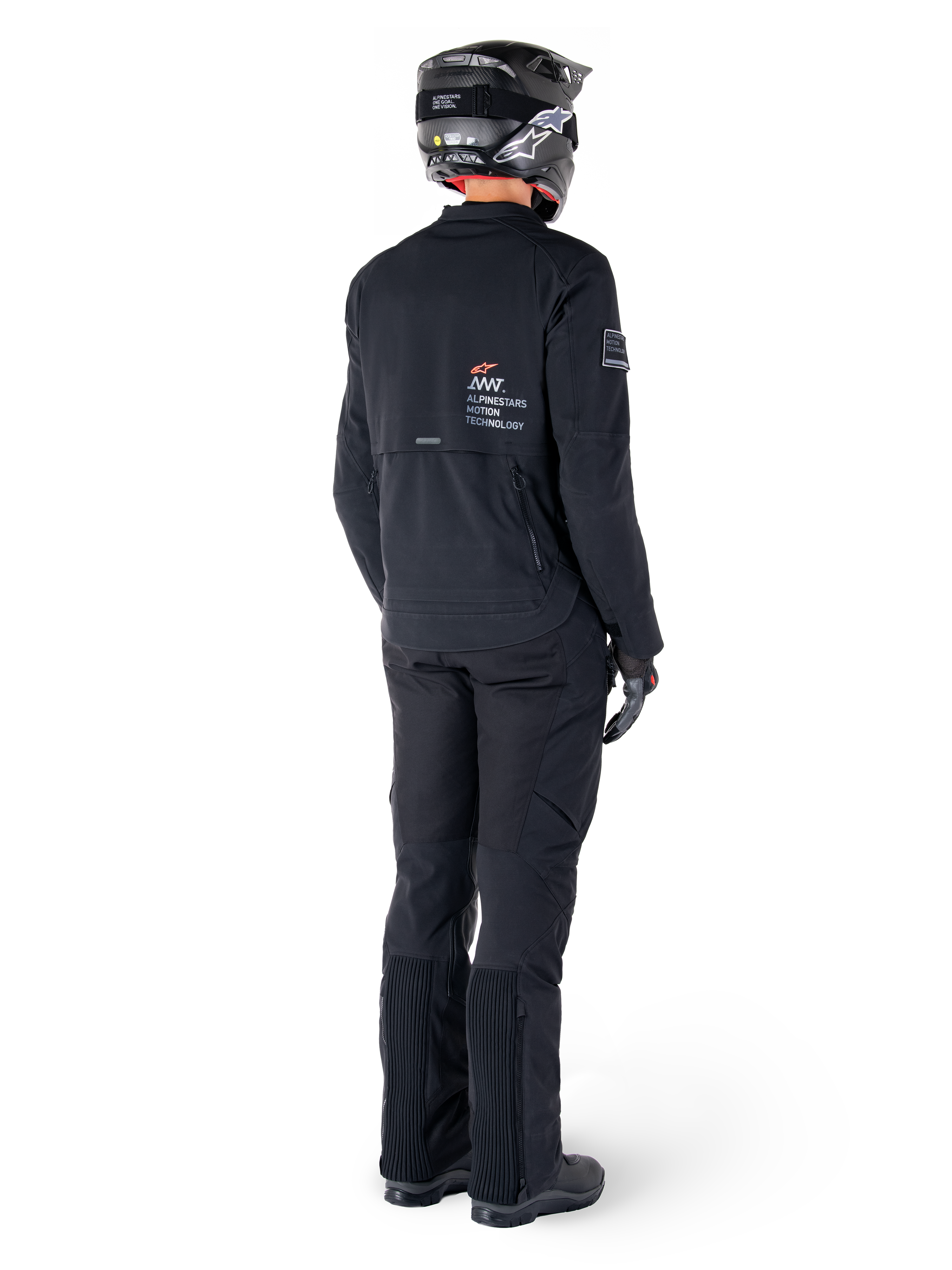 Kurtka Alpinestars AMT-8 Stretch Drystar® XF, czarna, widok z tyłu motocyklisty ubranego w kurtkę, pasujące czarne spodnie i czarny kask, z logo „Alpinestars Motion Technology” na plecach, techniczny elastyczny materiał do jazdy motocyklowej typu adventure