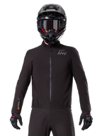Alpinestars AMT-8 Stretch Drystar® XF Liner, czarna wodoodporna podpinka motocyklowa, z zamkiem błyskawicznym z przodu i elastycznym pasem, logo AMT na piersi i brandingiem Drystar XF na rękawie, noszona z czarnym kaskiem i rękawicami.