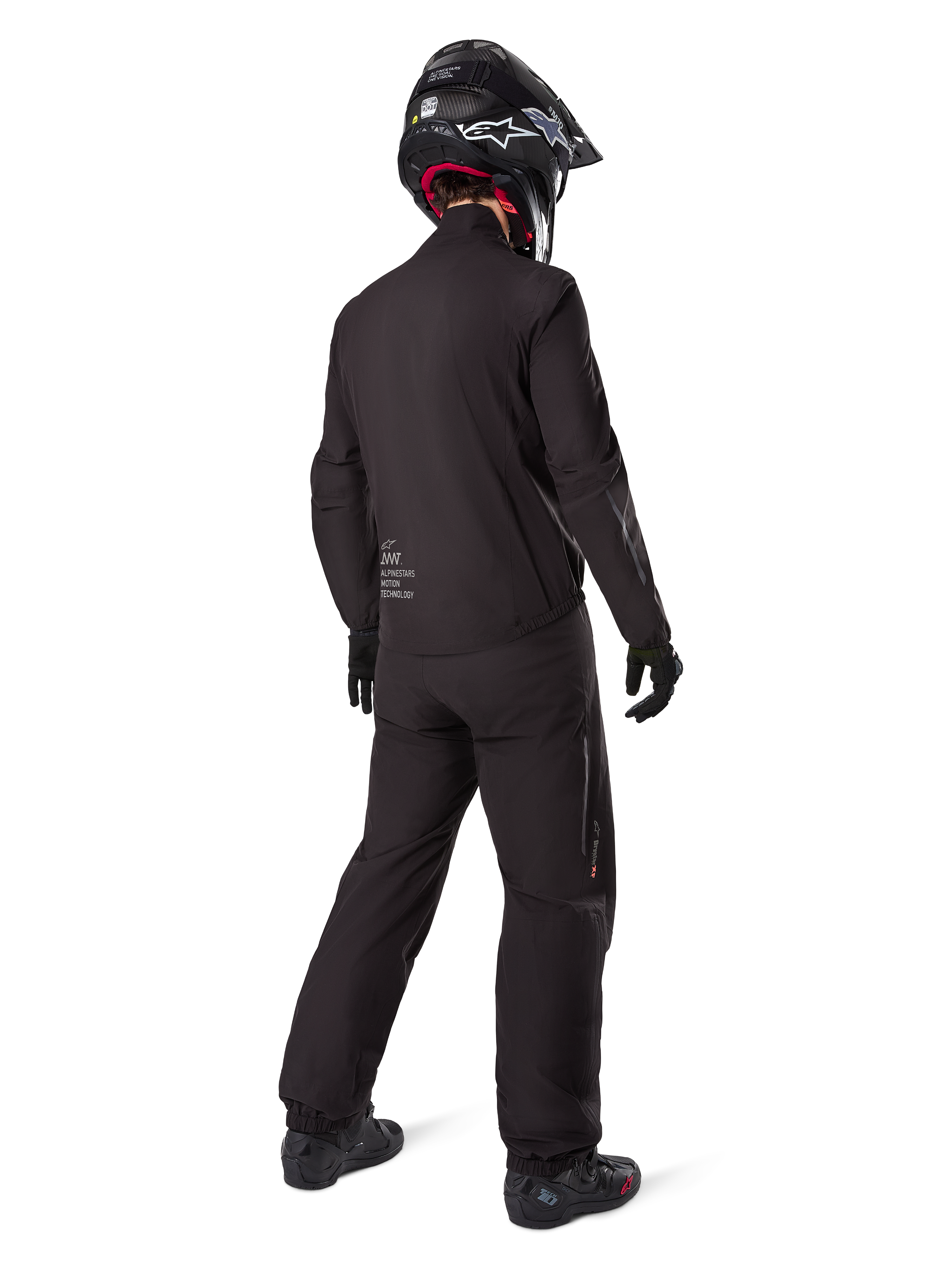 Widok z tyłu motocyklisty w podpince kurtki Alpinestars AMT-8 Stretch Drystar® XF, czarna techniczna odzież motocyklowa, noszona z pasującymi spodniami i czarnym kaskiem, logo „AMT Alpinestars Motion Technology” na plecach, minimalistyczny design do turystyki przygodowej