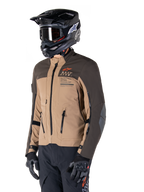 Kurtka Alpinestars AMT-8 Stretch Drystar® XF, motocyklowa kurtka adventure, ciemnobrązowa i ciemne khaki, noszona z czarnym kaskiem off-road i goglami, z logo Alpinestars Motion Technology i zamkami wentylacyjnymi