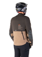 Kurtka Alpinestars AMT-8 Stretch Drystar® XF, motocyklowa kurtka adventure, ciemnobrązowa i ciemne khaki, widok z tyłu prezentujący branding AMT Alpinestars Motion Technology, dwukolorowa konstrukcja tekstylna z tylnymi zamkami wentylacyjnymi i wylotem powietrza o konstrukcji dachówkowej, zestawiona z czarnym kaskiem i spodniami motocyklowymi