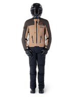 Kurtka Alpinestars AMT-8 Stretch Drystar® XF, kurtka motocyklowa adventure, ciemnobrązowa i ciemne khaki, noszona z czarnym kaskiem, goglami, czarnymi rękawicami, spodniami i butami, posiada otwory wentylacyjne na klatce piersiowej i branding AMT, dopasowany zestaw odzieży do turystyki przygodowej