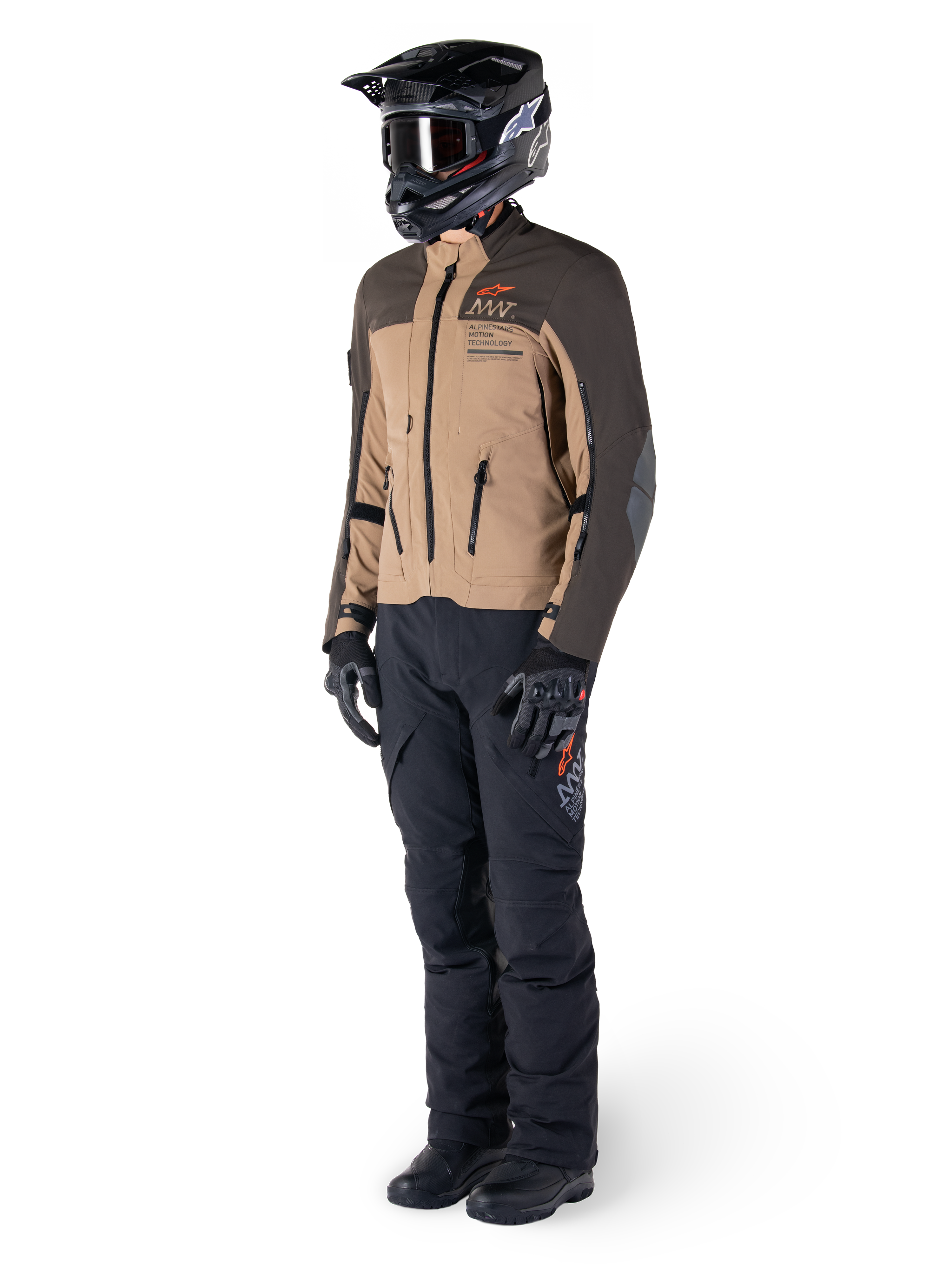 Motocyklista adventure w pełnym rynsztunku, kurtka Alpinestars AMT-8 Stretch Drystar® XF w kolorze ciemnobrązowym i ciemnym khaki, czarne spodnie adventure, czarny kask, rękawice i buty, pomarańczowe logo AMT oraz techniczne zamki wentylacyjne do turystyki długodystansowej