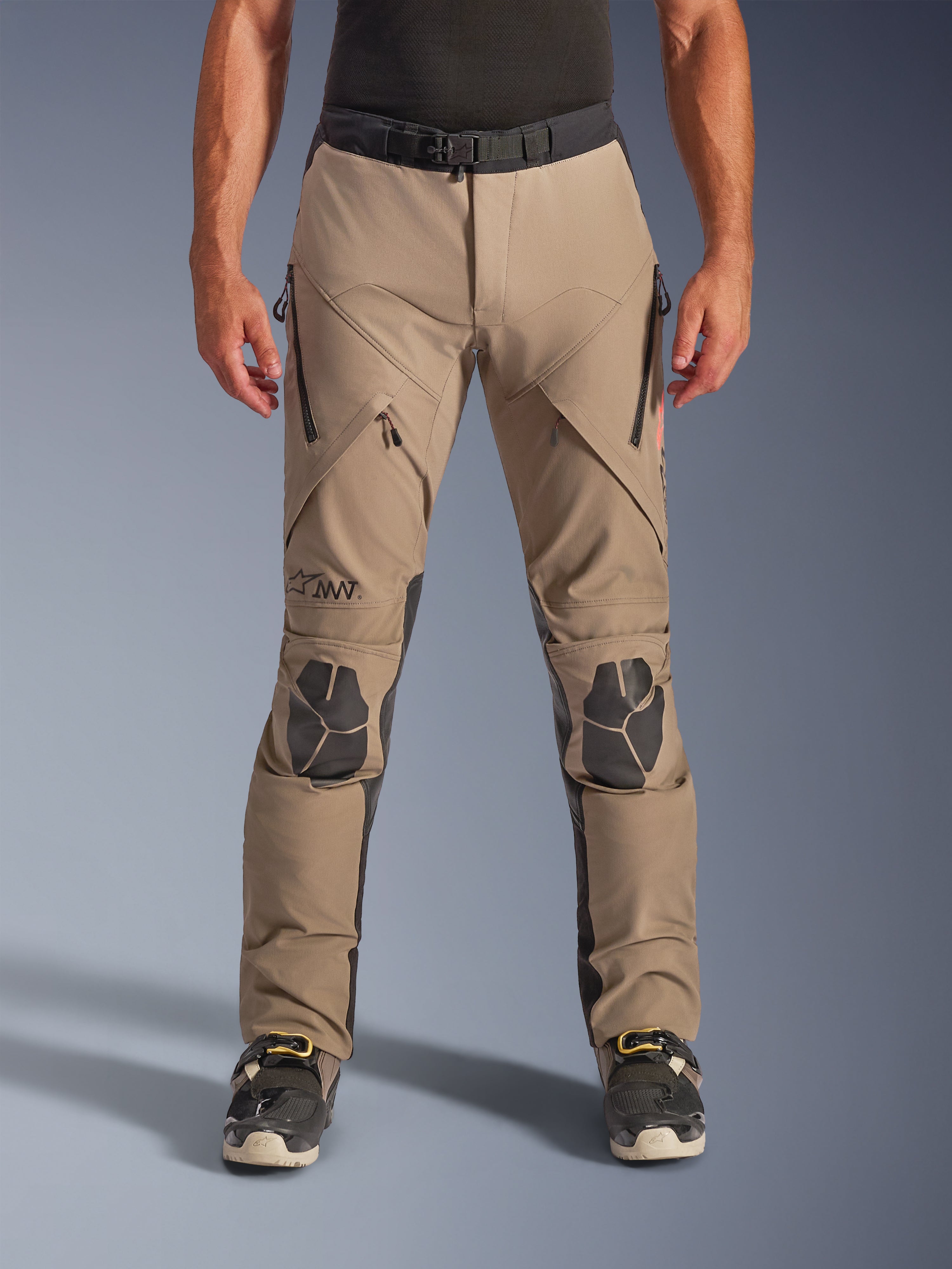 Spodnie Alpinestars AMT-8 Stretch Drystar® XF, motocyklowe spodnie adventure w kolorze Walnut Black, z zapinanymi na zamek otworami wentylacyjnymi na udach, czarnymi wzmocnionymi panelami na kolanach i magnetycznym zapięciem w pasie, zaprojektowane do profesjonalnej turystyki przygodowej.