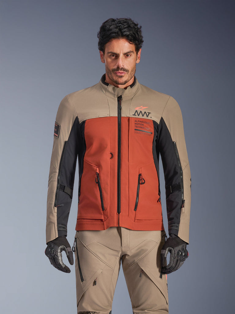 Alpinestars AMT-8 Stretch Drystar® XF Jacket, kurtka adventure touring w kolorze Walnut Rust Black, noszona przez modela z pasującymi spodniami i rękawicami, trójkolorowy design w kolorach beżowym, rdzawym i czarnym z brandingiem AMT na klatce piersiowej, dopasowanie active touring do jazdy motocyklem