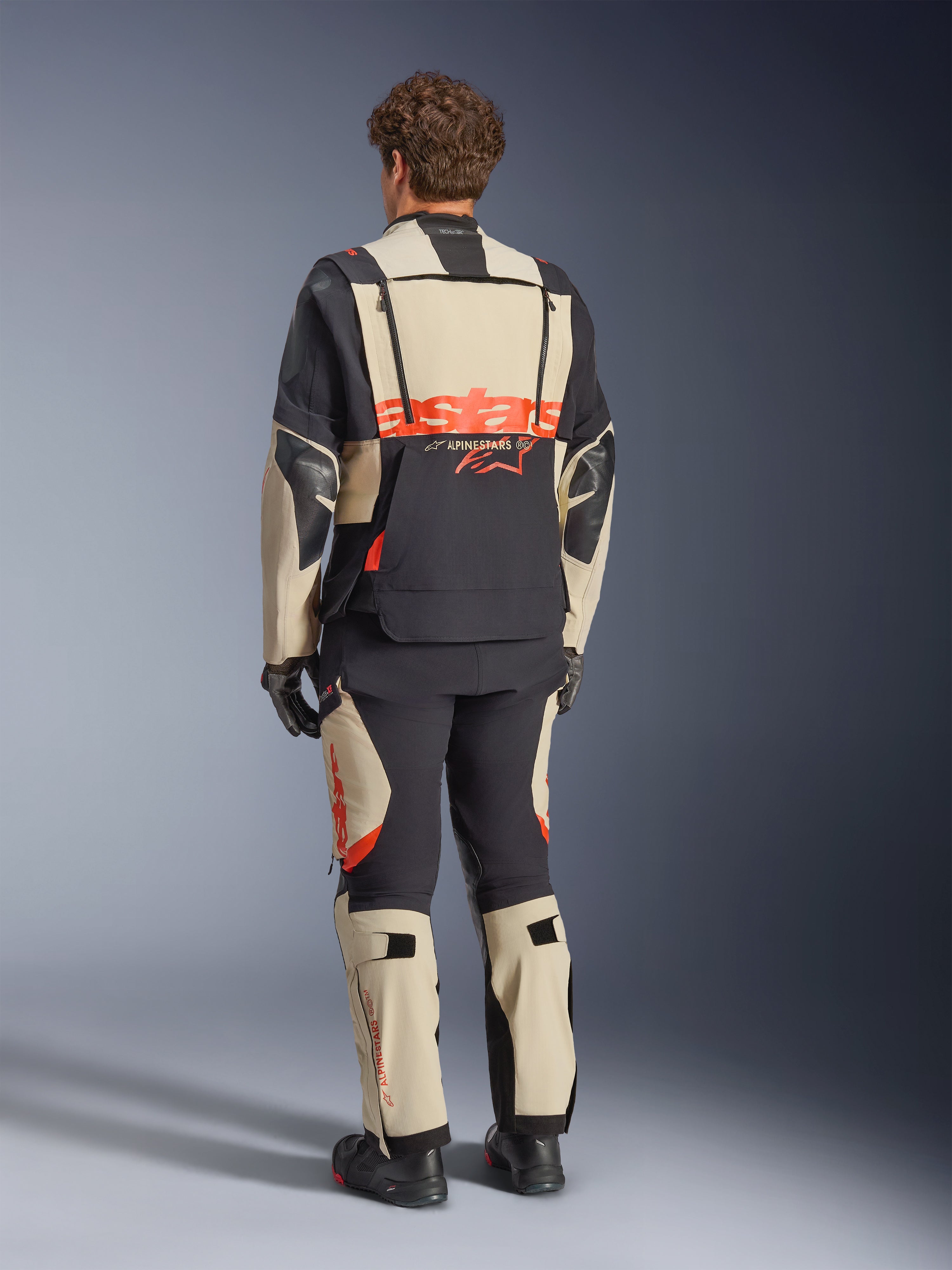 Alpinestars Halo Pro Drystar® XF Laminated Jacket, Mastic Black, back view, adventure motorcycle jacket with large orange 'astars' branding across the rear, worn with matching technical pants and boots, modular design for versatile terrain