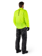 Osoba widoczna od tyłu ubrana w kurtkę Alpinestars Hurricane Rain V2 w kolorze Yellow Fluo i spodnie Hurricane Rain V2 w kolorze czarnym, pionowe logo na plecach kurtki, wodoodporna motocyklowa odzież przeciwdeszczowa, czarne rękawice i buty