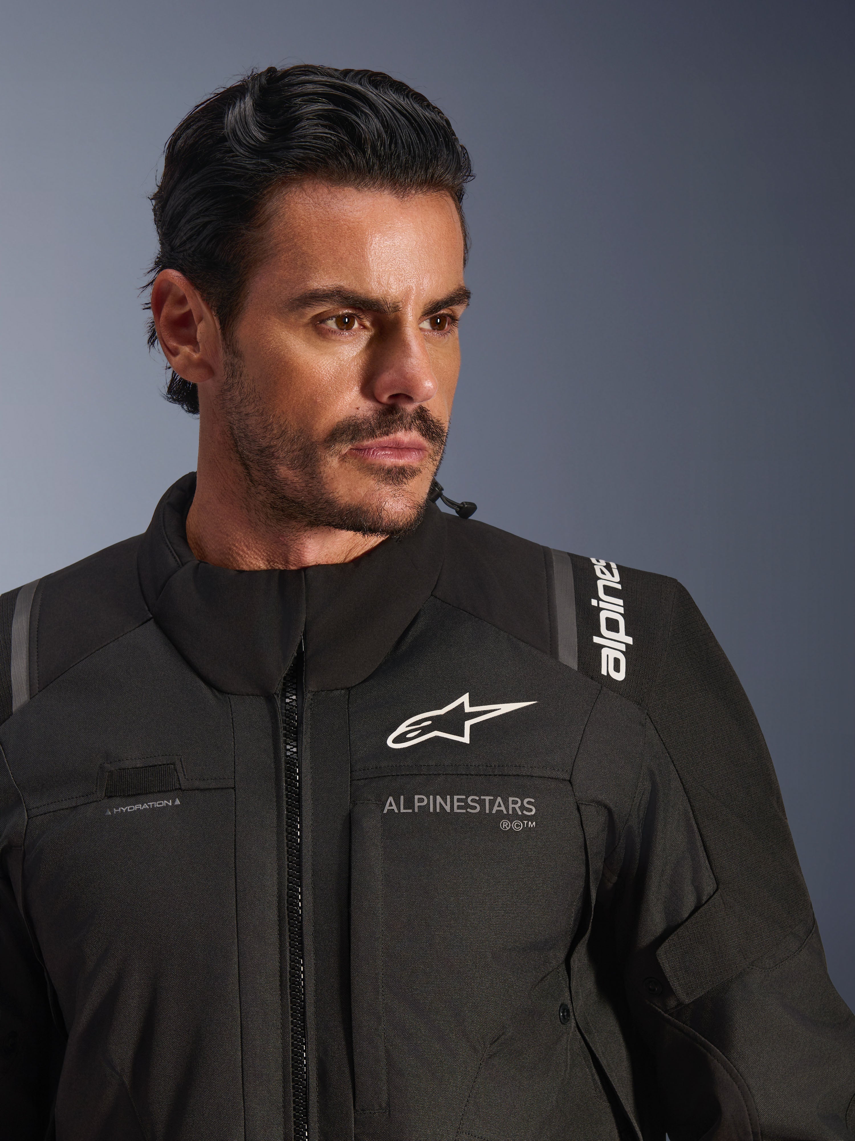 Kurtka Alpinestars Andes V4 Drystar®, czarna, prezentowana przez modela, zbliżenie na klatkę piersiową i ramiona, białe logo Alpinestars, materiał tekstylny z detalami wentylacyjnymi i pętlą na wąż nawadniający, motocyklowa odzież adventure-touring