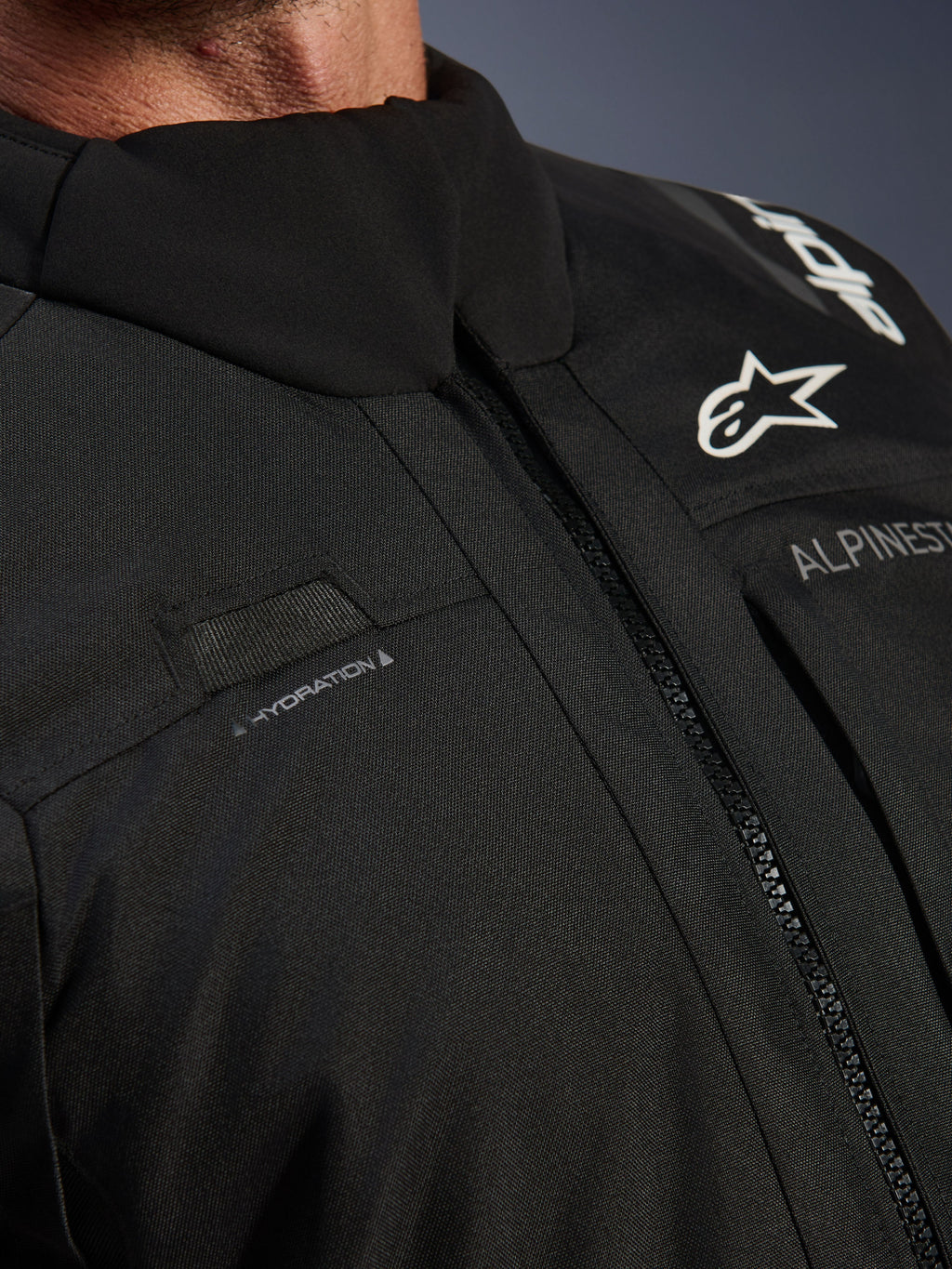 Kurtka Alpinestars Andes V4 Drystar®, czarna, zbliżenie na detale klatki piersiowej z pętlą na wąż nawadniający, wodoodporny przedni zamek VISLON® oraz logo Alpinestars na wytrzymałym materiale tekstylnym
