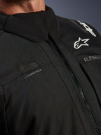 Kurtka Alpinestars Andes V4 Drystar®, czarna, zbliżenie na detale klatki piersiowej z pętlą na wąż nawadniający, wodoodporny przedni zamek VISLON® oraz logo Alpinestars na wytrzymałym materiale tekstylnym
