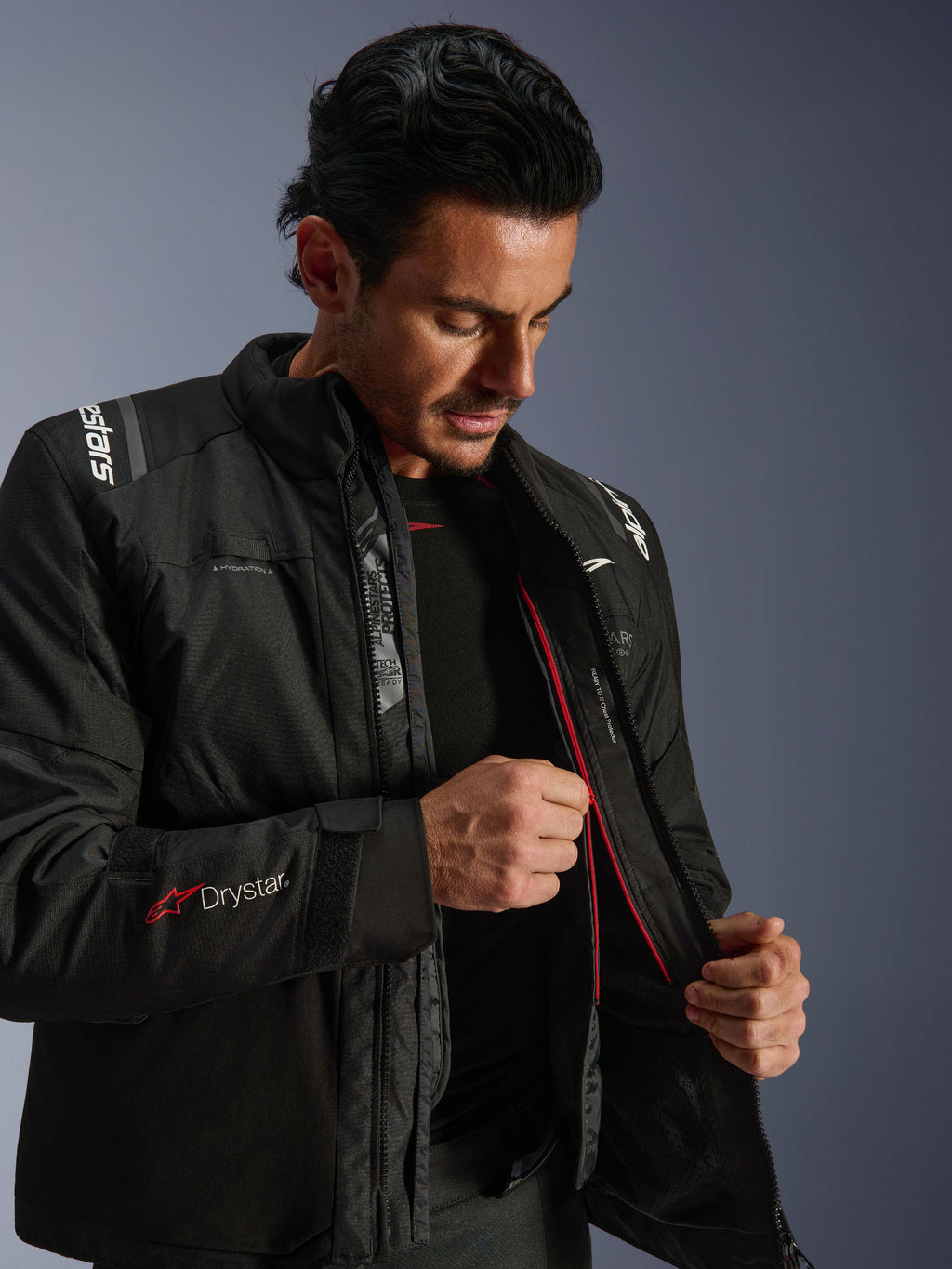 Kurtka Alpinestars Andes V4 Drystar®, czarna motocyklowa kurtka adventure, mężczyzna prezentujący wewnętrzną podszewkę termiczną i czerwony zamek, logo Drystar® na rękawie, wytrzymały materiał tekstylny do jazdy w każdych warunkach pogodowych