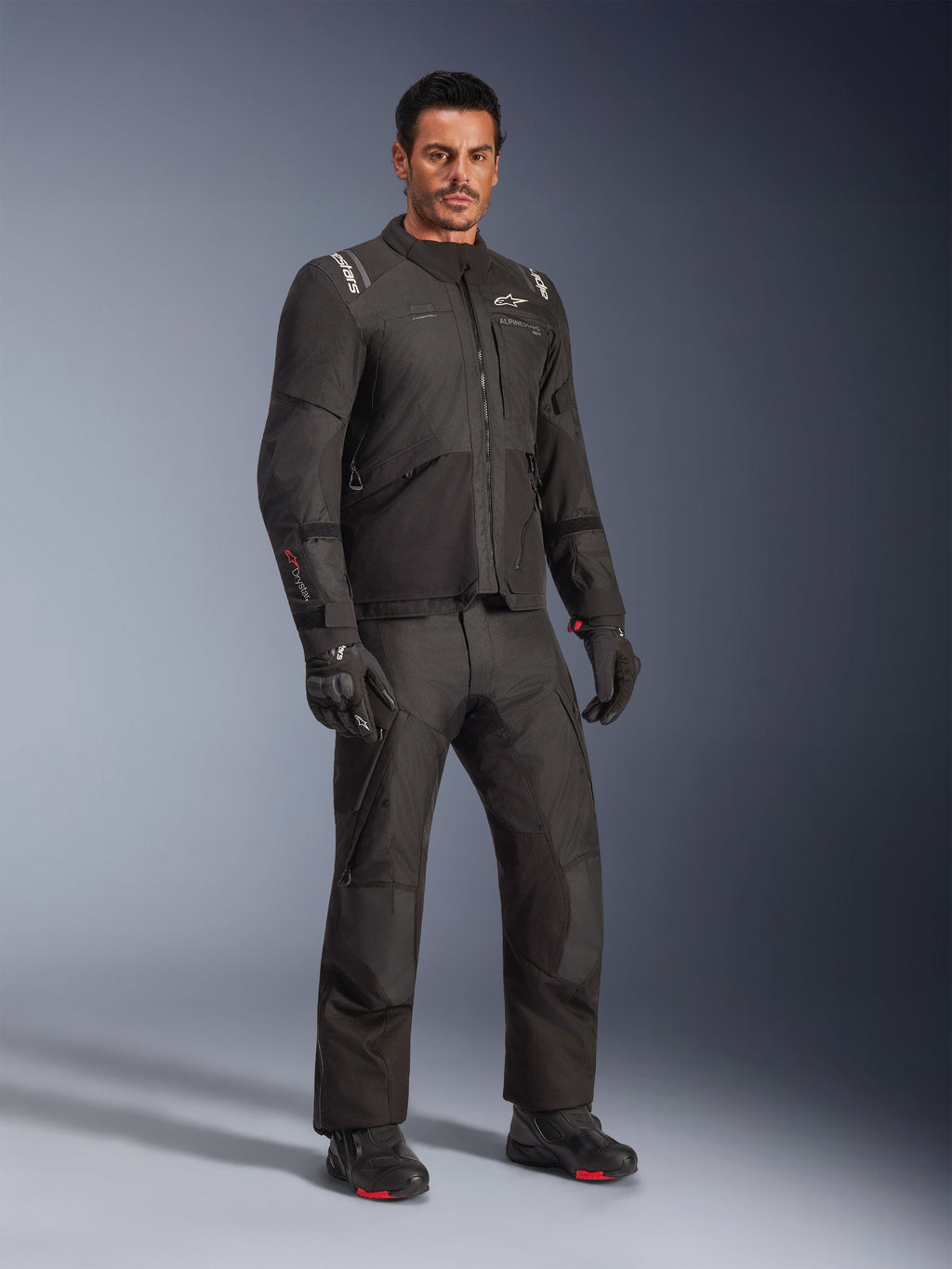 Kurtka Alpinestars Andes V4 Drystar®, czarny zestaw odzieży motocyklowej na modelu, tekstylna kurtka i spodnie adventure-touring, czarne rękawice i buty, zdjęcie studyjne, nowoczesny design do jazdy w każdych warunkach pogodowych