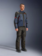 Męski model w kurtce Alpinestars Andes V4 Drystar® w kolorystyce Night Navy i Mood Indigo z czarnymi panelami i czerwonymi akcentami, zestawionej z czarnymi spodniami i butami motocyklowymi, techniczna odzież adventure touring w studio.